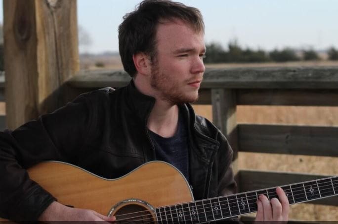 Connor Standridge - NWU Man playing acoustic guitar outdoors in natural setting.