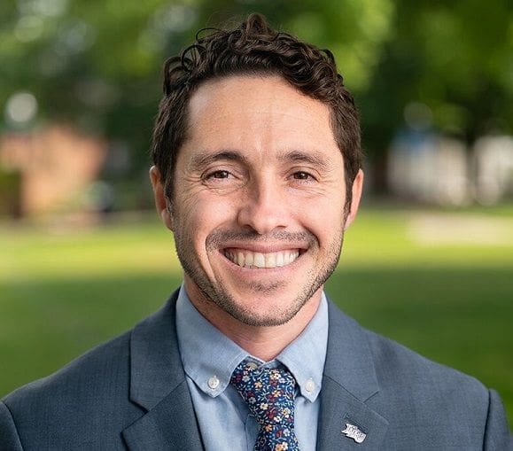 Corey Esquenazi Smiling man in suit with floral tie outdoors.