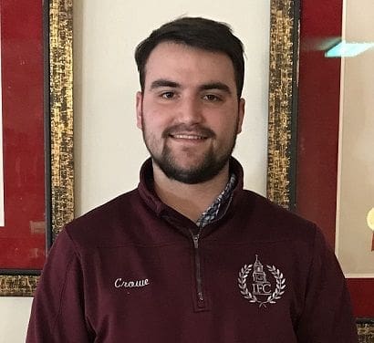 Young man in maroon jacket smiling indoors.