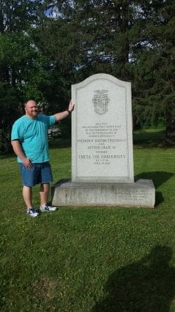 Man standing beside a historical monument in a park.