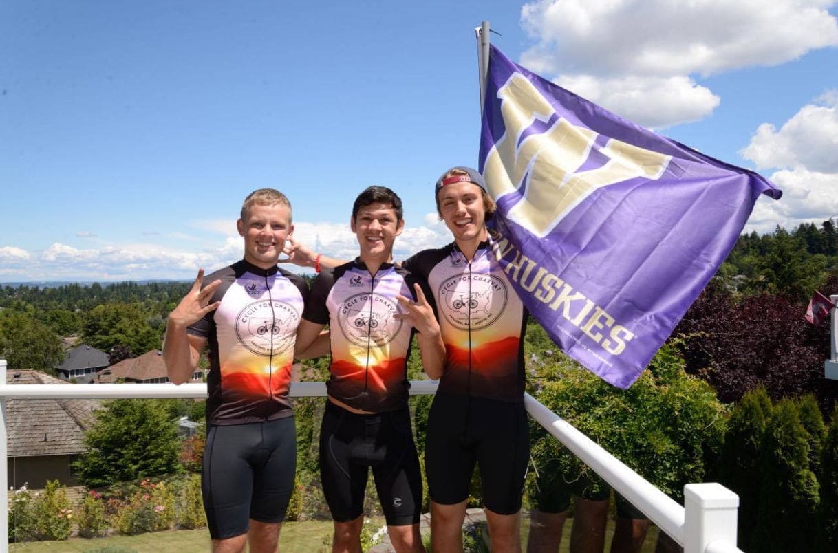 Three cyclists celebrating with a Huskies flag.