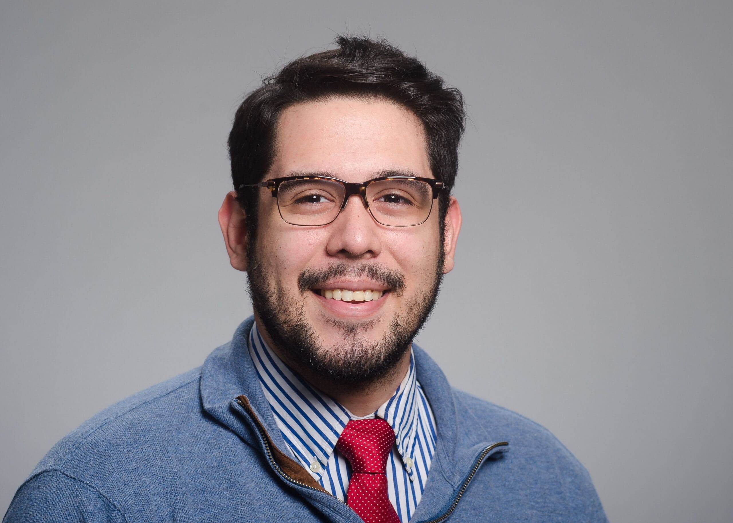 Daniel Mendoza Smiling man in glasses wearing a blue sweater.