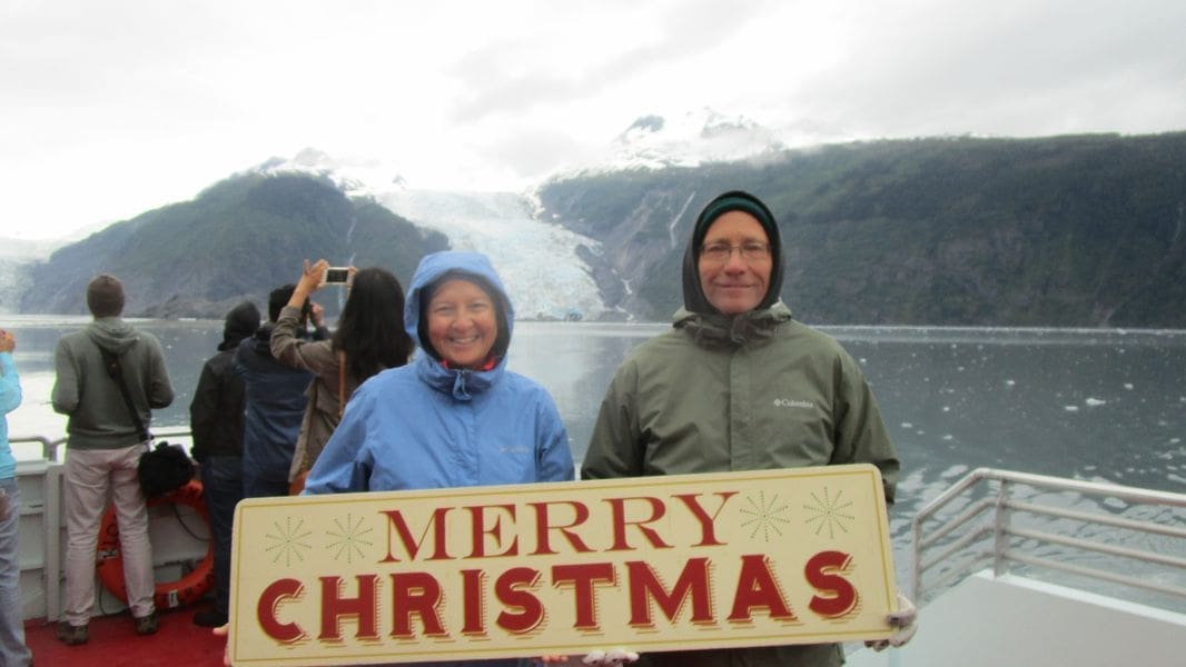Couple holding Merry Christmas sign near glacier.