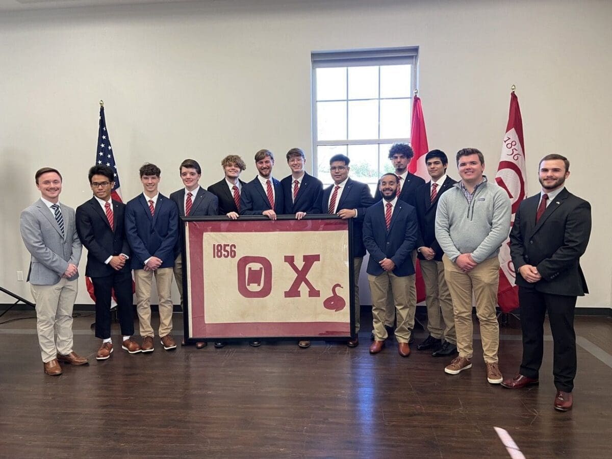 Group of men posing with a banner in a hall.