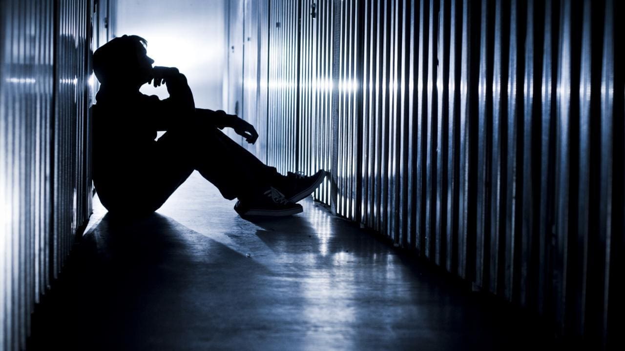 Silhouette of person sitting against a corridor wall.