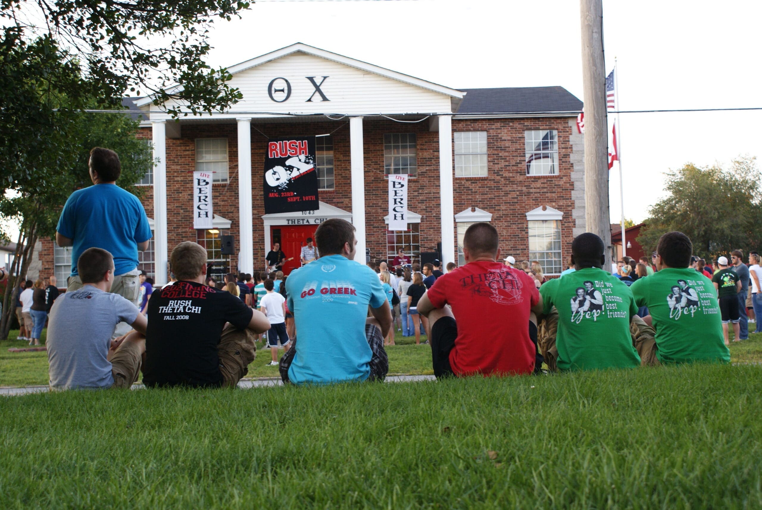 Students sitting in front of a fraternity house.