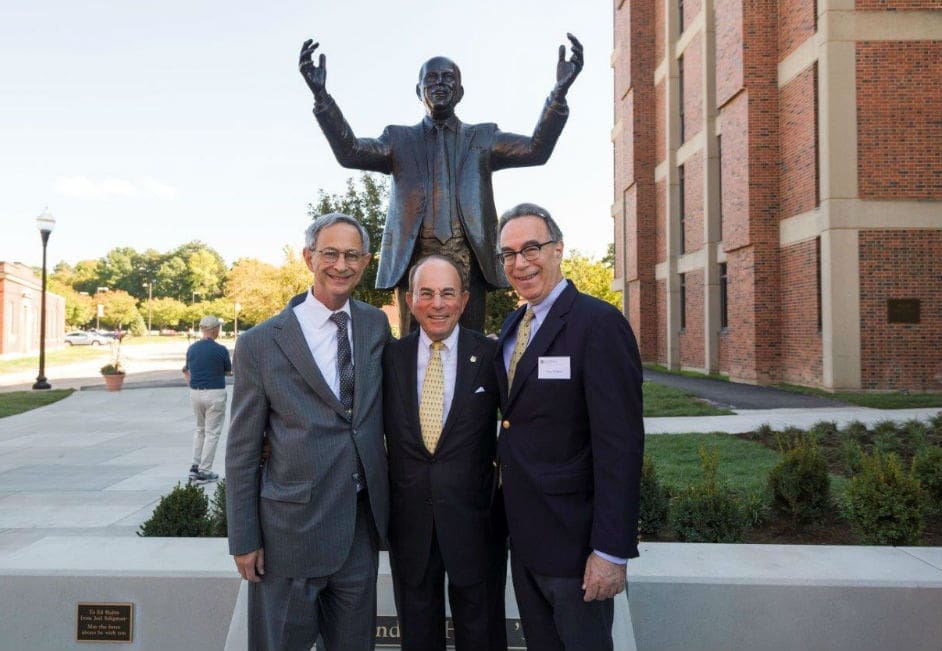 Three men posing near a statue outdoors.
