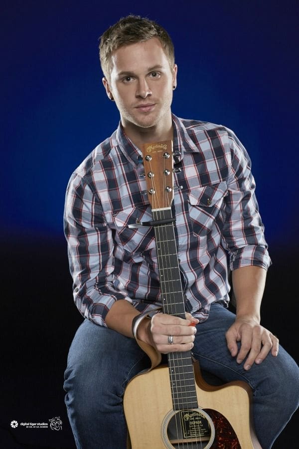 Man sitting with guitar against dark background.