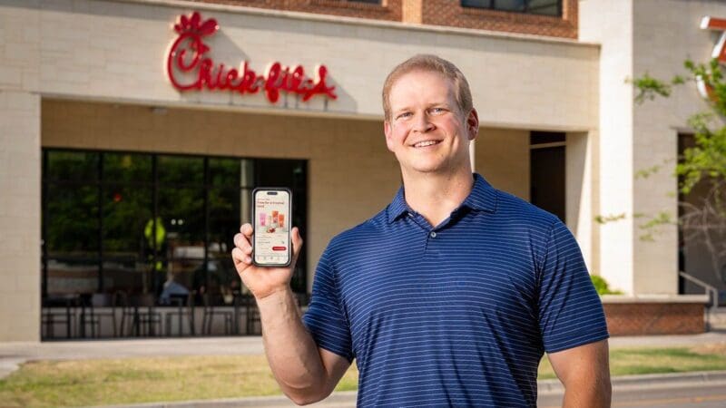 Man holding smartphone outside Chick-fil-A restaurant.