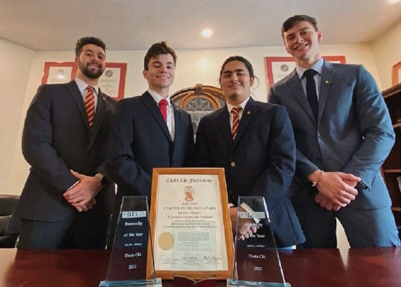 Four young men in suits with awards and certificates.
