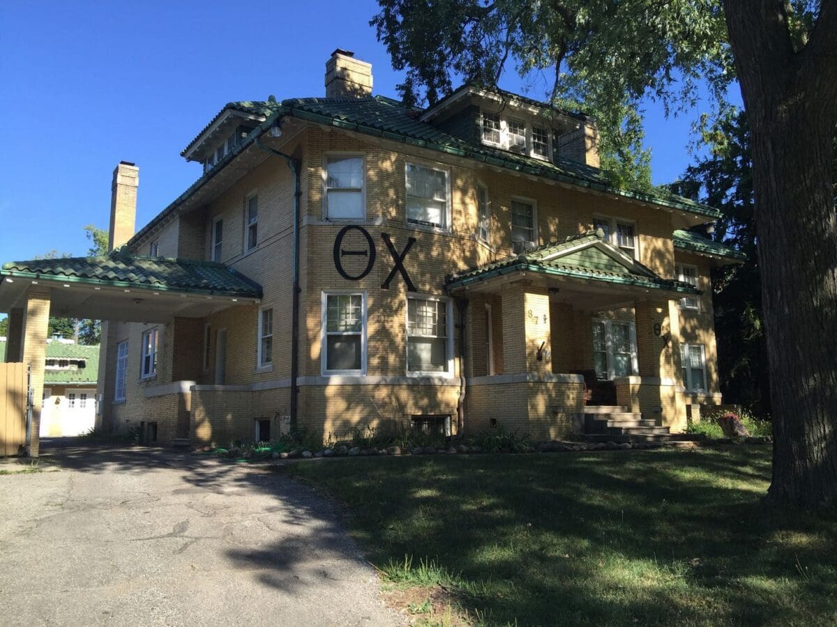 Historic yellow house with green roof and porch.