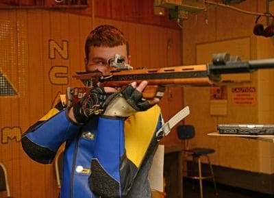 Young shooter aiming with a precision rifle indoors.