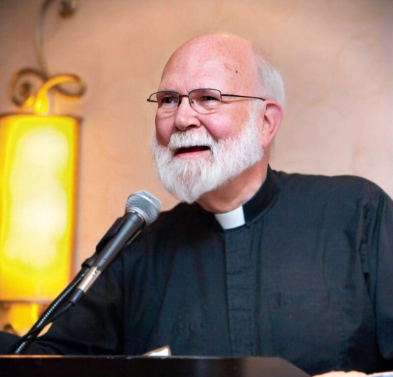 Smiling priest speaking at a microphone event.