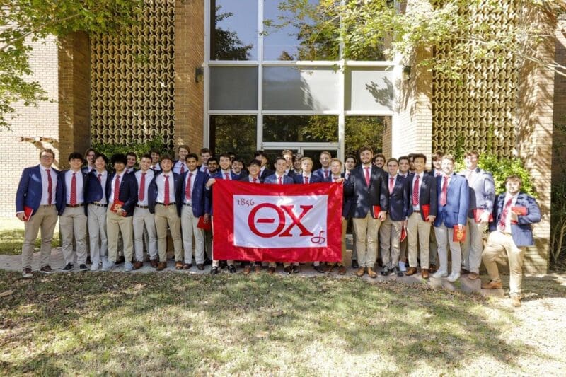 Group of fraternity members holding a banner outdoors.