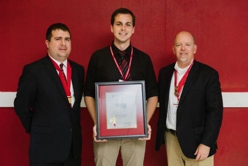 Three men posing with an award certificate.