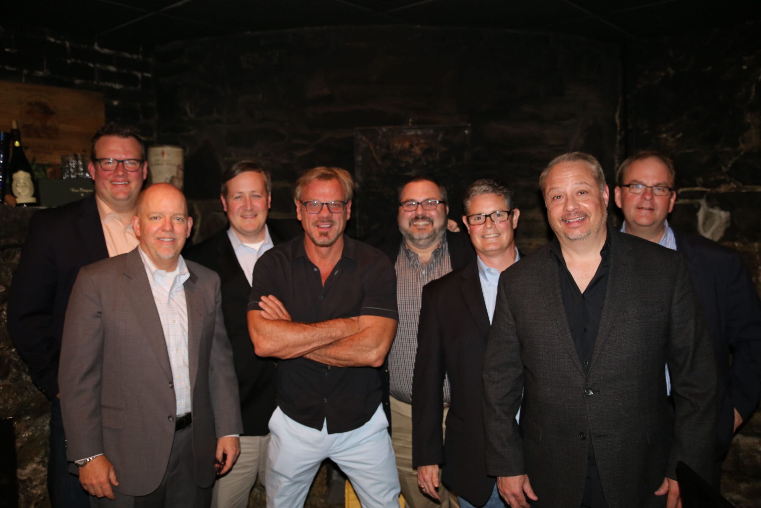 Group of men posing together in a dimly lit setting.