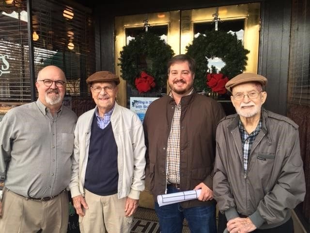Four men posing outside decorated entrance.