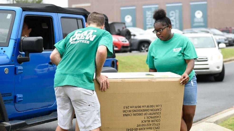 Iota Xi/Georgia College Article Volunteers lifting a large cardboard box together.