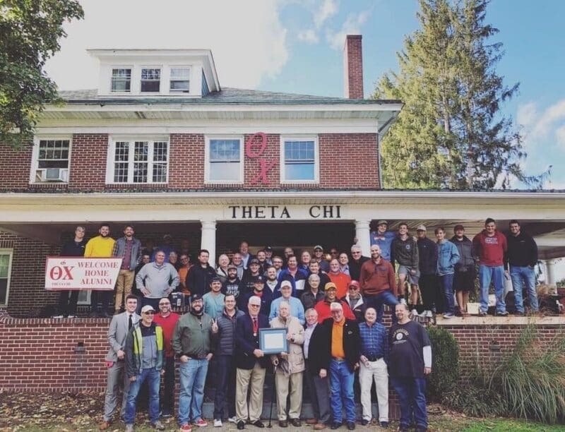 Theta Chi fraternity reunion group photo outside house.