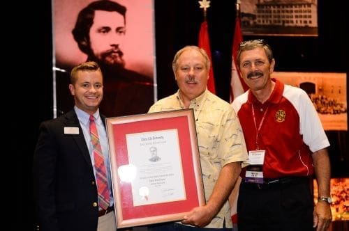 Three men holding an award certificate at an event.