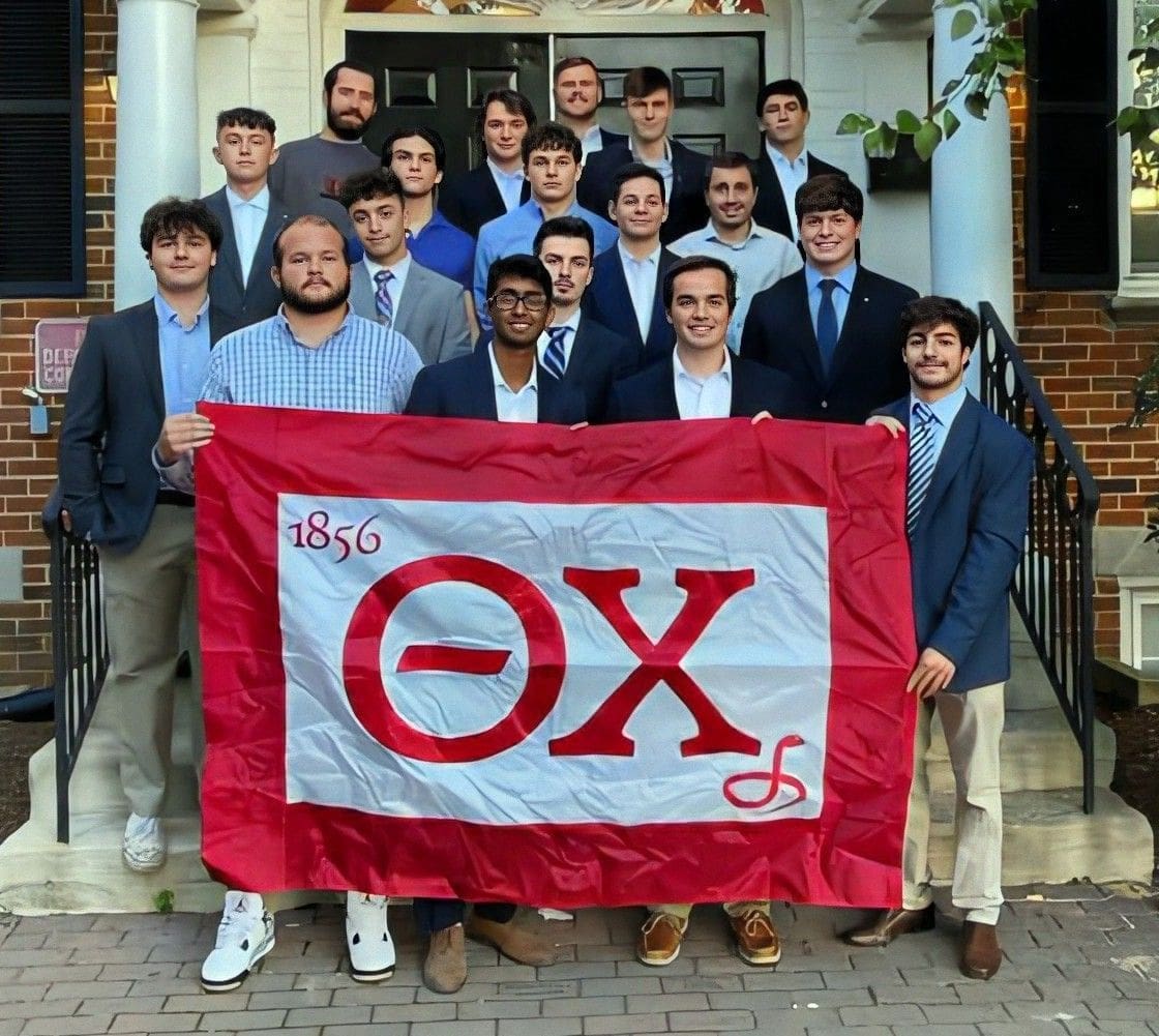 Group of fraternity members holding flag outside building.