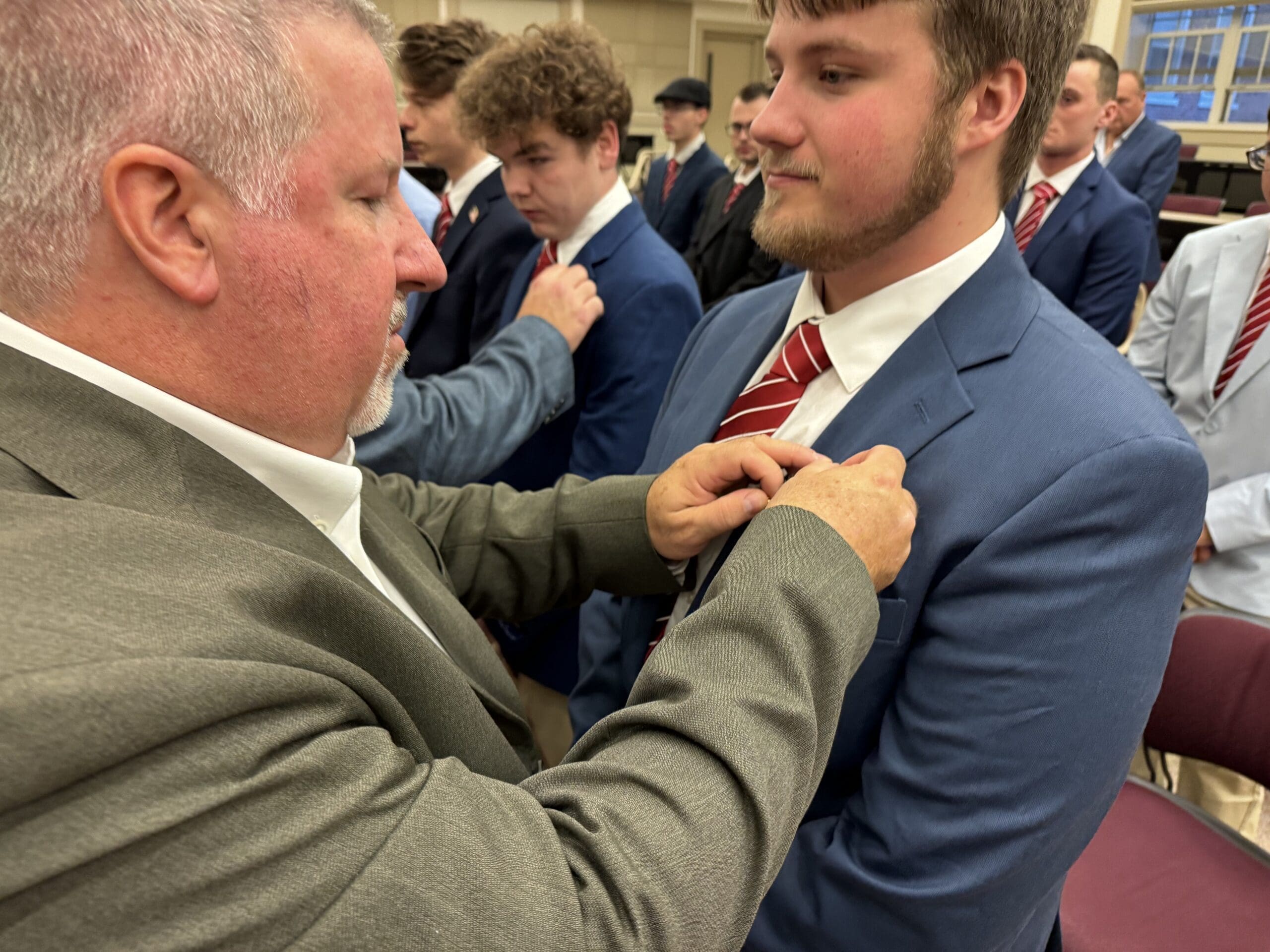 Man adjusting tie on young man at event.