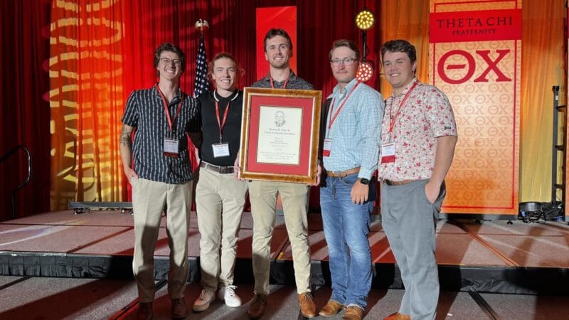 Group of five men holding an award at event.