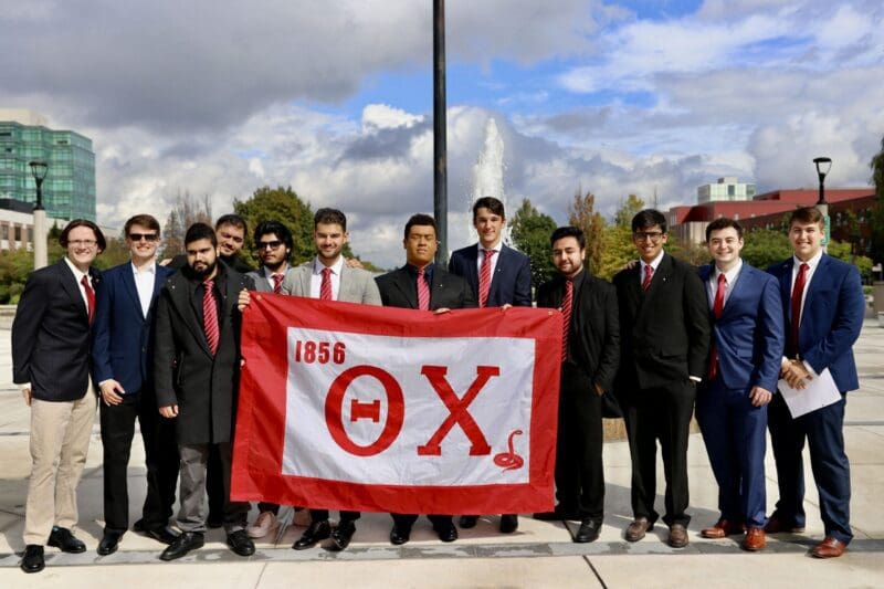 Group of men holding a fraternity flag outdoors.