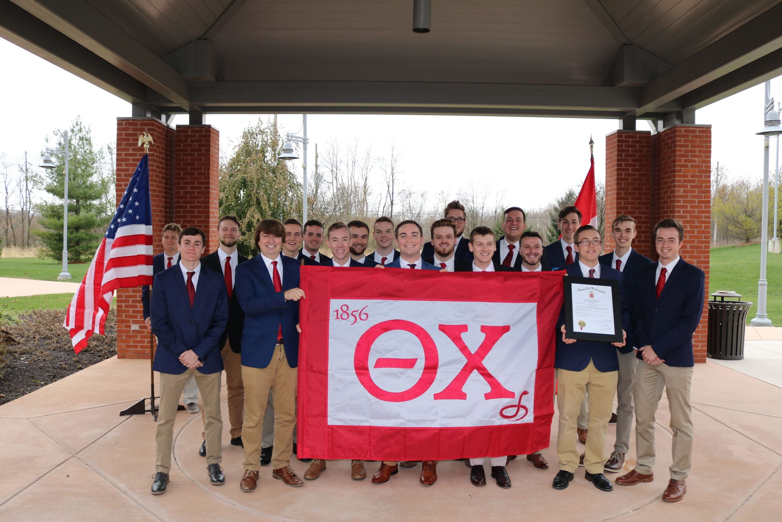 Group of students holding Omega Chi flag outdoors.