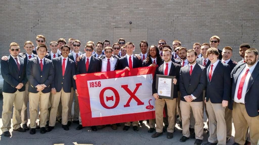 Group of fraternity members holding a flag and certificate.