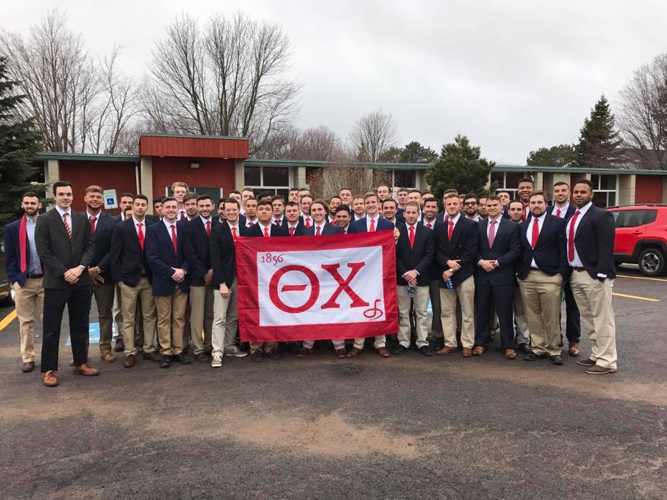 Group of fraternity members holding a banner outdoors.