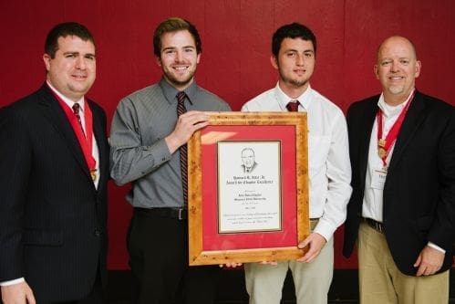 Four men holding an award plaque together.