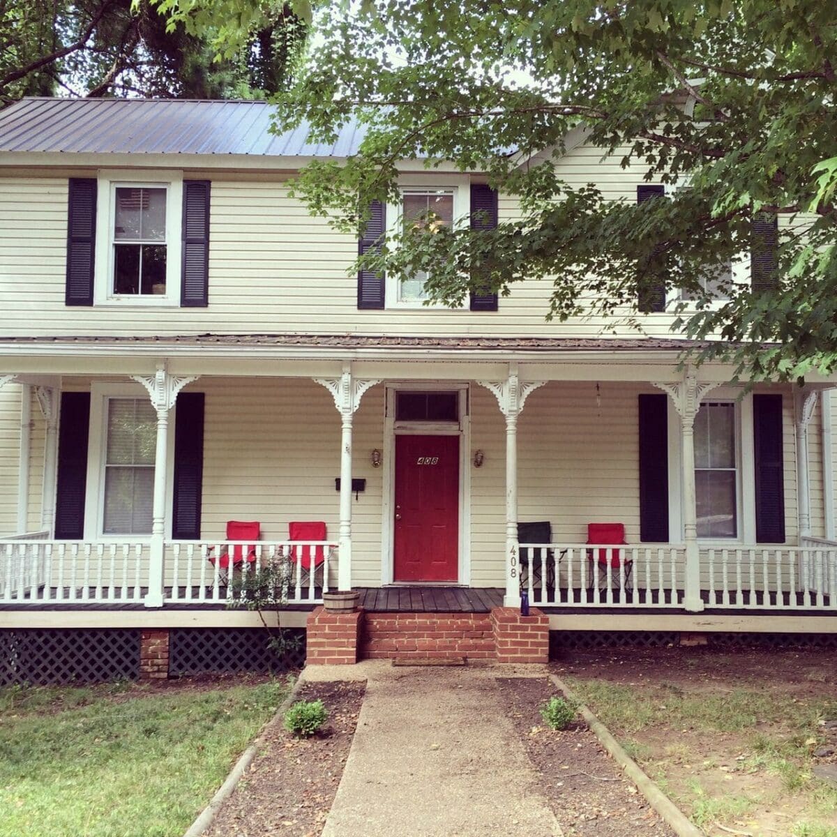 Historic house with red door and porch seating.