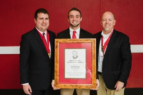 Three men holding an award plaque together.