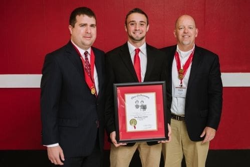 Three men holding an award certificate at an event.