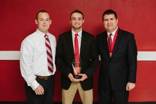 Three men posing with an award trophy.