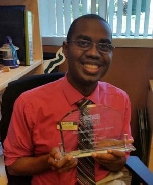 Smiling man holding an award in office setting.