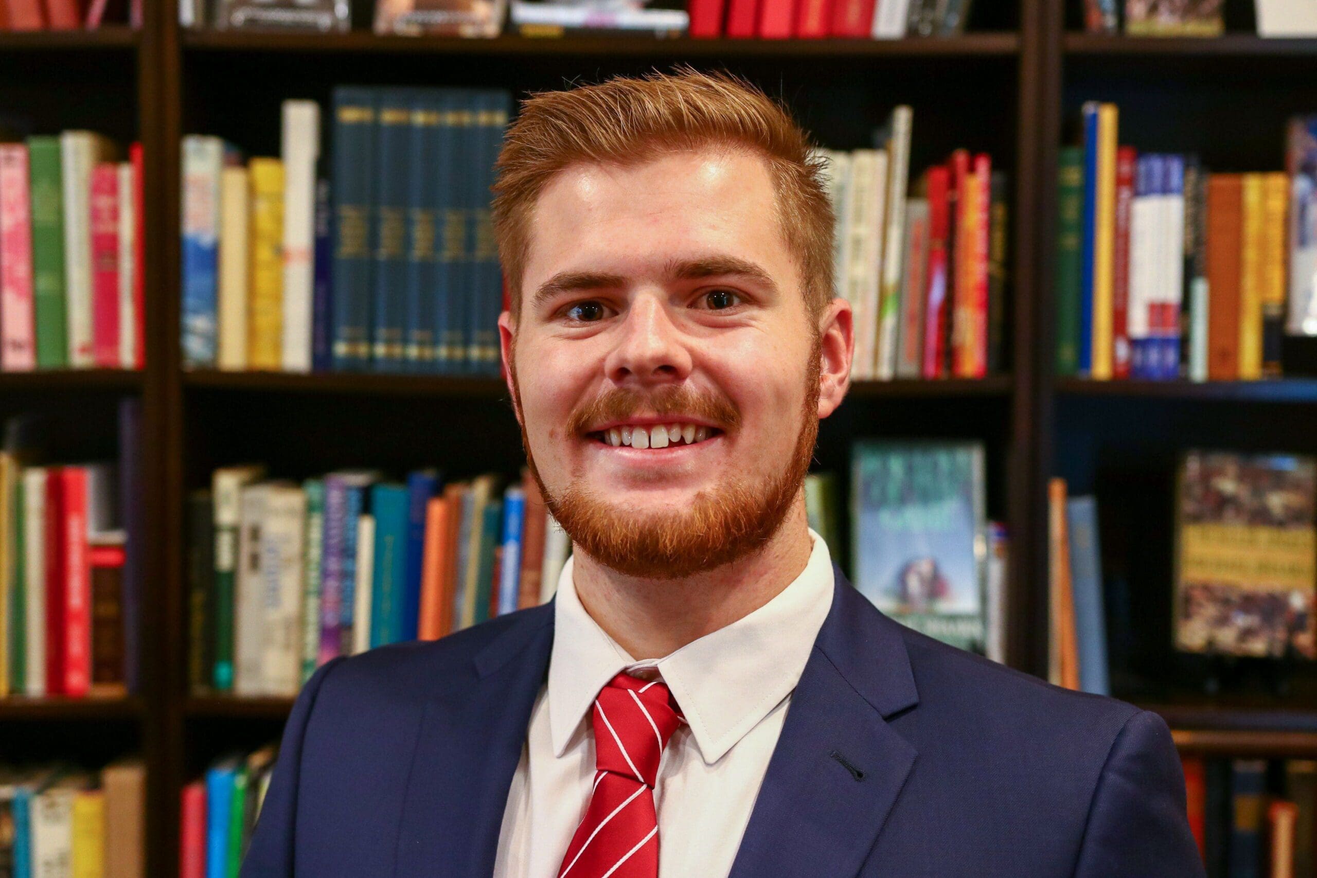 Smiling man in suit with bookshelf background.