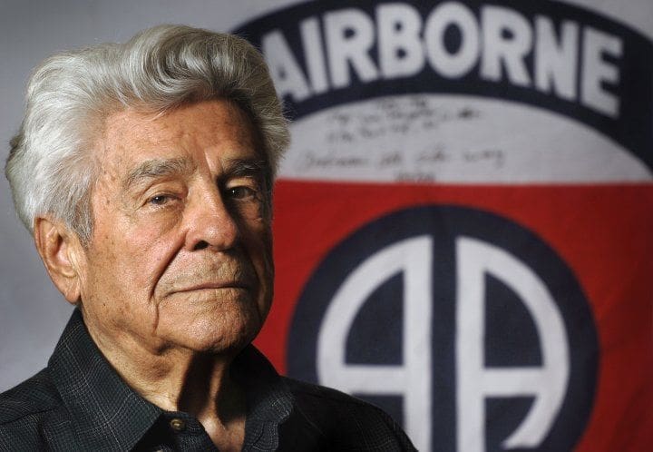 Elderly man with Airborne insignia in background.