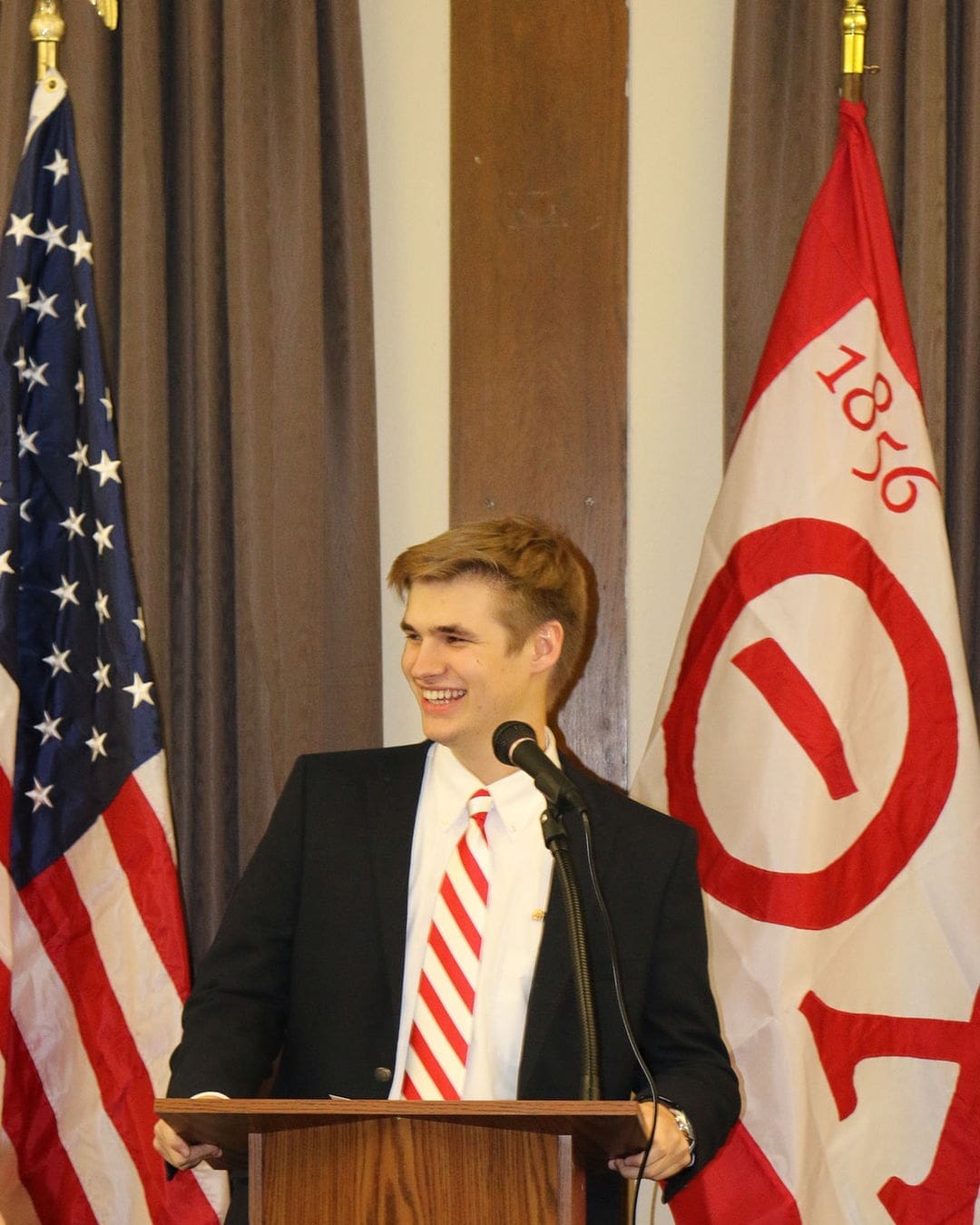 Jared Pinkerton Smiling speaker at podium with flags behind him.