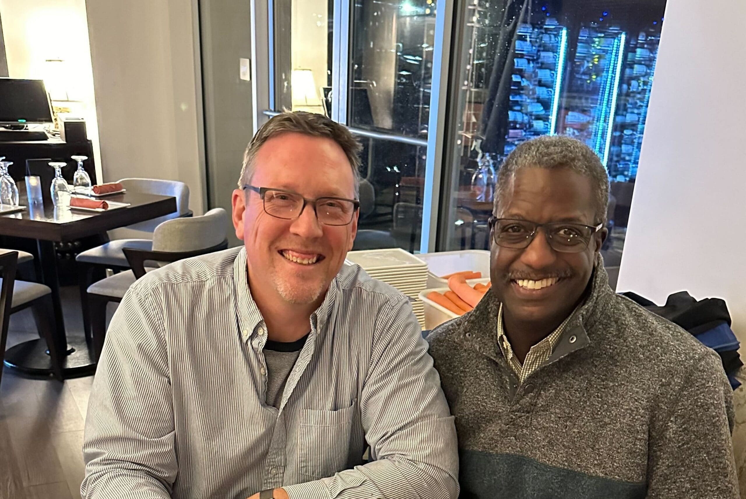 Two smiling men sitting at a table together.