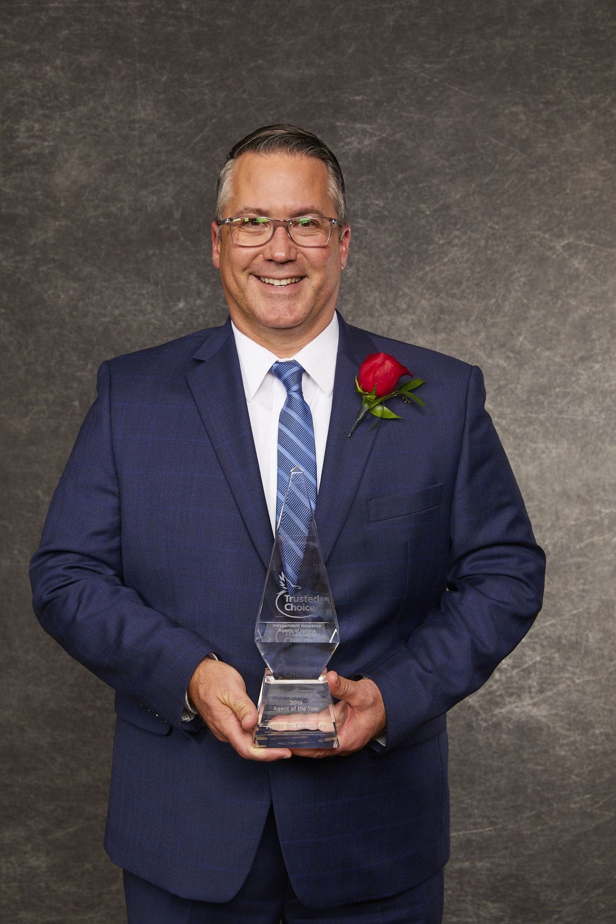 Smiling man in suit holding an award trophy.