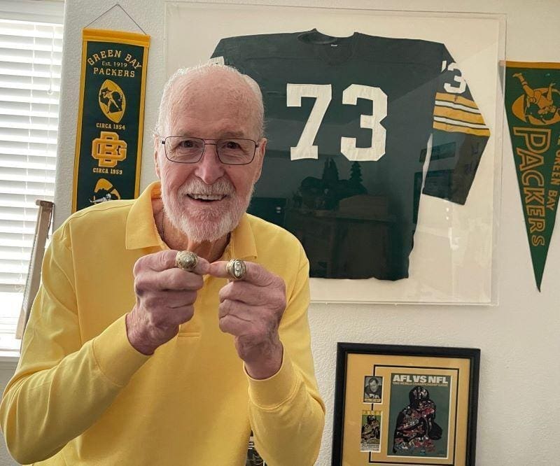Elderly man with championship rings and Packers memorabilia.