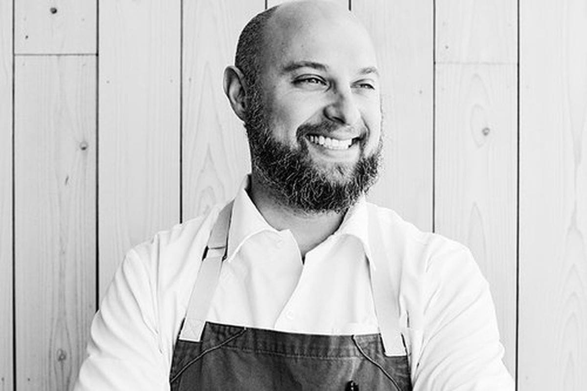 Jorge Guzman Smiling chef wearing an apron against wooden background.
