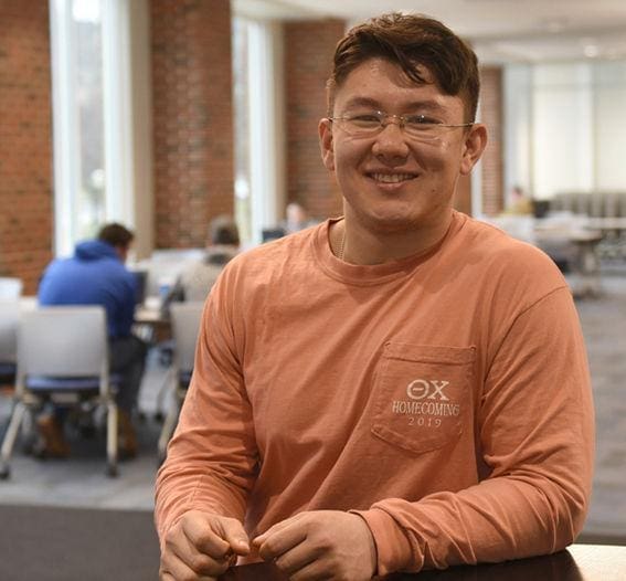 Kaelin Yi Smiling student in study area wearing glasses.