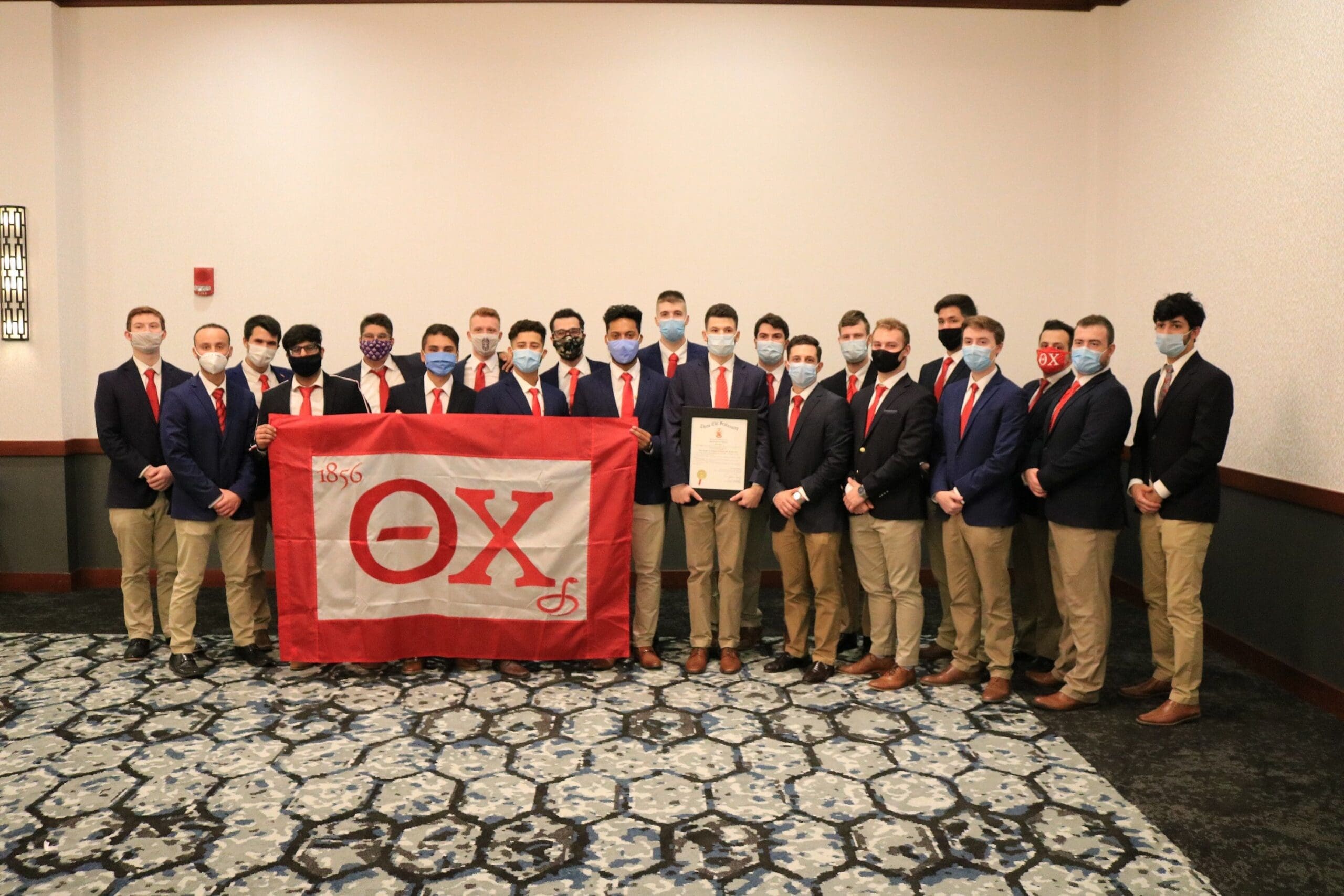 Kappa Xi - Albany Group of men in suits with fraternity flag.