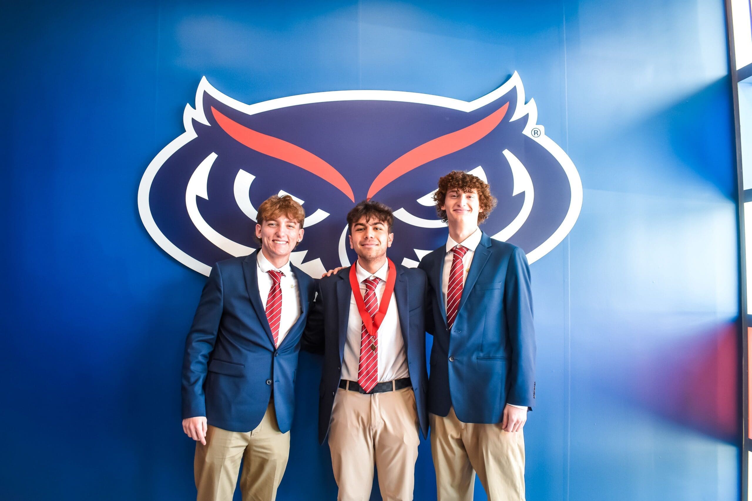 Three young men in suits pose with owl logo.