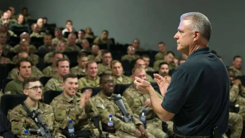 Military personnel listening to a speaker in a theater.