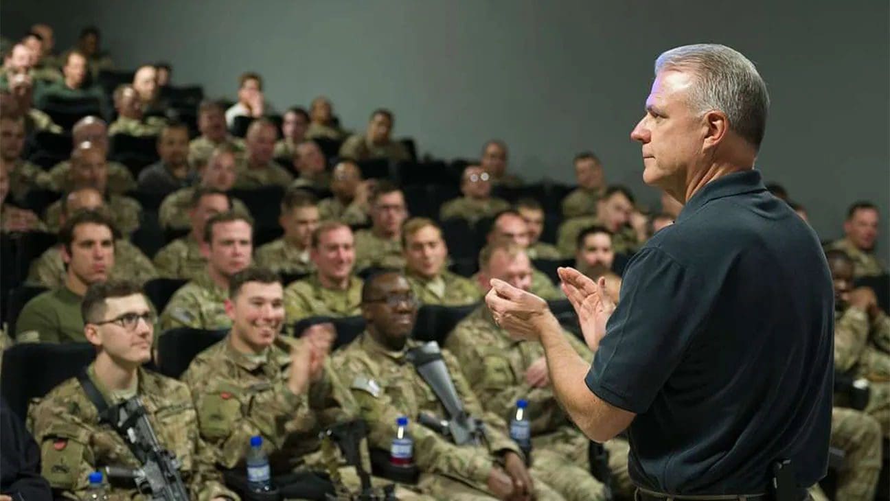 Military personnel listening to a speaker in a theater.