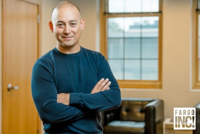 Kevin Tobosa Smiling man in blue sweater, arms crossed indoors.